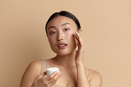 Asian Woman Applying Cream. Female With Fresh Skin Holding Cream Bottleの写真素材