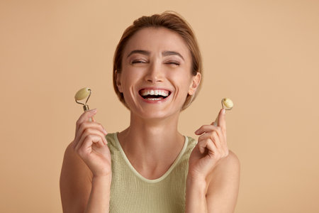 Face massage. Laughing Woman Posing With Jade Facial Roller for Skin Careの写真素材