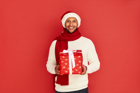 Happy Man Holding Present. Multiracial Guy in Santa Hat Holding Present Boxの写真素材