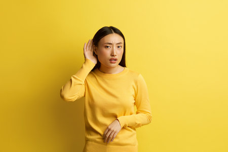 Asian Woman Trying to Hear Isolated. Confused Girl Keeping Hand Near Earの写真素材