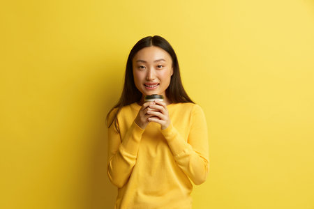 Smiling Woman Holding Coffee to Go. Friendly Asian Woman Warming Up with Coffeeの写真素材