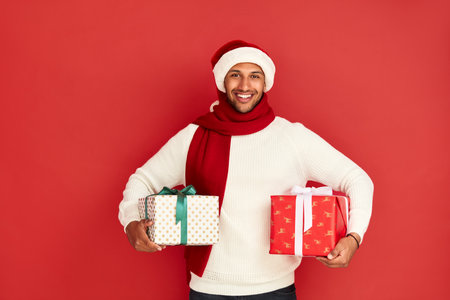 Smiling Man Holding Presents. Positive Guy in Santa New Year Hat Holding Boxesの写真素材