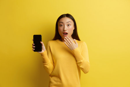 Surprised Woman Holding Smartphone. Shocked Girl Standing and Holding Mobileの写真素材