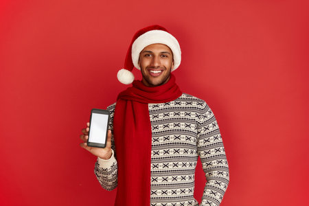 Happy Man Using Smartphone. Multiracial Guy Santa Hat Smiling Showing Cellphoneの写真素材
