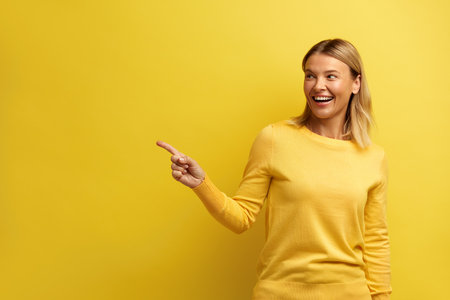 Happy Woman Pointing Aside. Pretty Female Smiling Toothy, Isolated on Yellowの写真素材