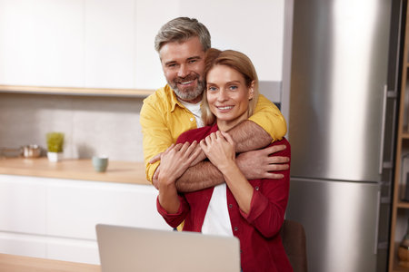 Happy Couple Embracing At Kitchen. Middle Aged Spouses Cuddling At Homeの写真素材