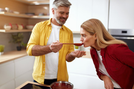 Couple Cooking At Kitchen. Senior Man Feeding Woman From Spoonの写真素材