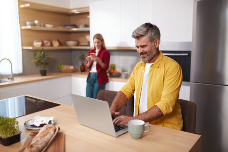 Senior Man Using Laptop At Kitchen. Happy Couple Spending Weekend Togetherの写真素材