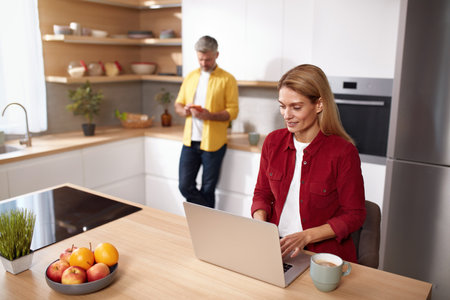 Blonde Woman Using Laptop At Kitchen. Happy Couple Spending Weekend Togetherの写真素材