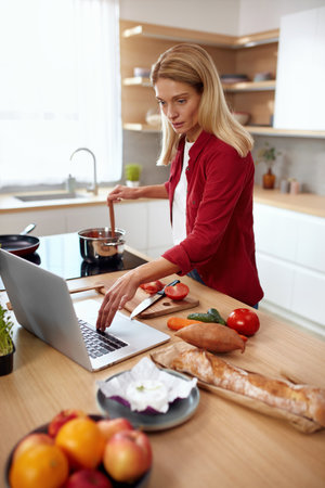 Healthy Woman Cooking At Kitchen. Beautiful Senior Lady Looking Laptop Recipesの写真素材