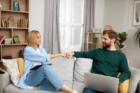 Couple Using Gadgets At Home. Married Couple Of Freelancers Bumping Handsの写真素材