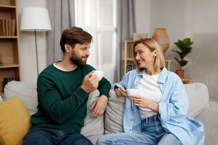 Happy Couple Drinking Coffee At Home. Young Couple Talking And Holding Cupsの写真素材
