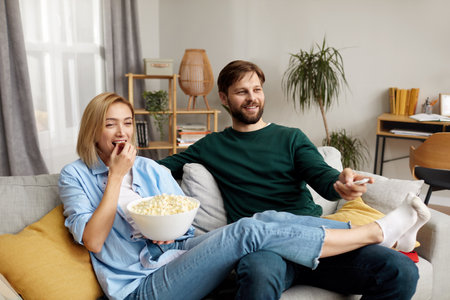 Laughing Couple Watching TV At Home. Loving People Resting On Sofaの写真素材