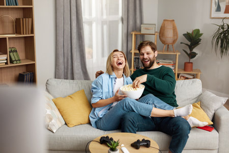 Laughing Couple Watching TV At Home. Loving People Resting On Sofaの写真素材