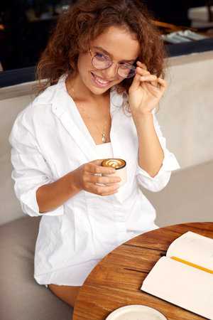 Woman At Cafe. Happy Girl In Casual Clothes And Glasses Holding Coffeeの写真素材