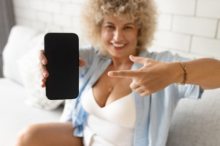 Curly Woman Pointing at Smartphone Screen with Joyの写真素材
