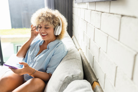Joyful Woman Enjoying Music on Sofa with Smartphone and Headphonesの写真素材
