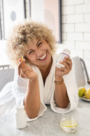 Smiling Woman in Bathrobe Holding Supplements at Homeの写真素材