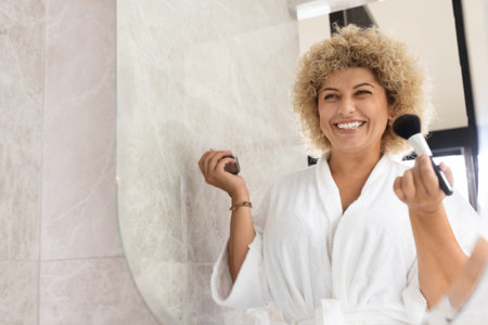 Smiling Woman in Bathrobe Applying Makeup During Morning Routineの写真素材