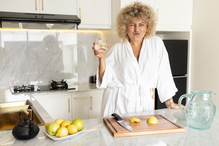 Woman in White Robe Making Lemon Water in Modern Kitchenの写真素材