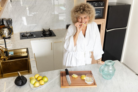Happy Woman in Bathrobe Enjoying Fresh Lemon in Modern Kitchenの写真素材
