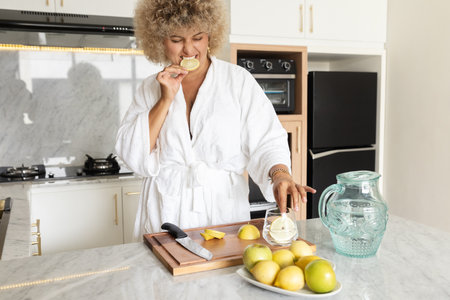 Woman in White Bathrobe Enjoying Fresh Lemon in Modern Kitchenの写真素材