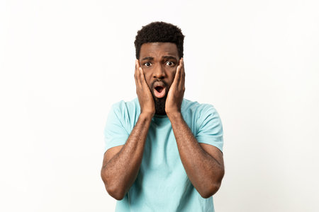 Shocked Young Man with Hands on Face over White Backgroundの写真素材