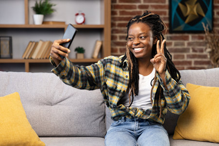 Woman Enjoying Video Call at Home, Smiling and Gesturing Peace Signの写真素材