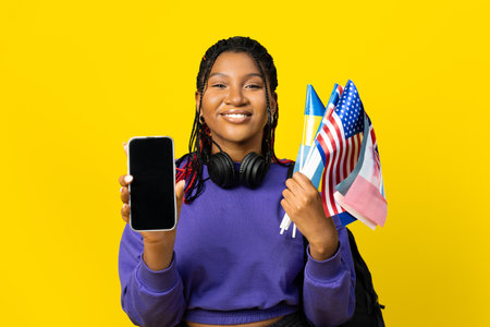 Student Showing Smartphone and Holding Flags on Yellow Backgroundの写真素材