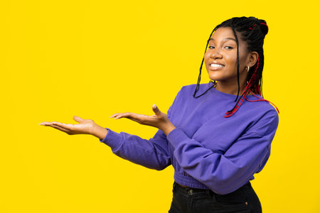 Confident Woman Presenting Product on Yellow Backgroundの写真素材