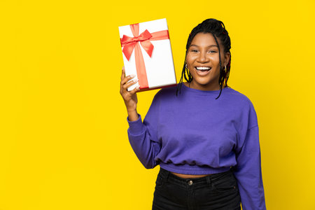 Woman Holding a White Gift Box on Yellow Backgroundの写真素材