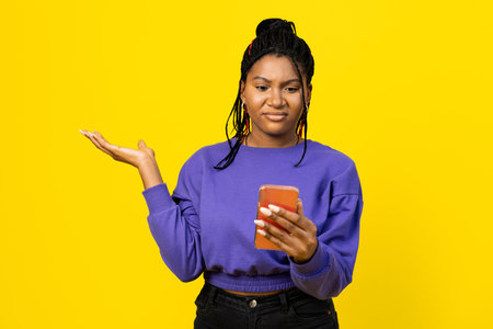 Woman Puzzled by Smartphon on Yellow Backgroundの写真素材
