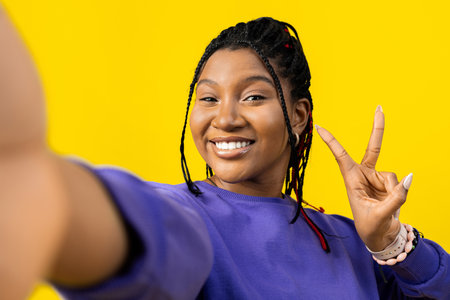 Woman Taking Selfie with Peace Sign on Yellow Backgroundの写真素材
