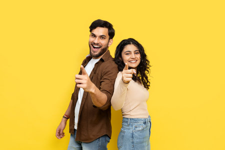 Happy Couple Pointing Towards Camera on Yellow Backgroundの写真素材