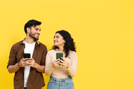 Young Couple Using Smartphones On Yellow Backgroundの写真素材