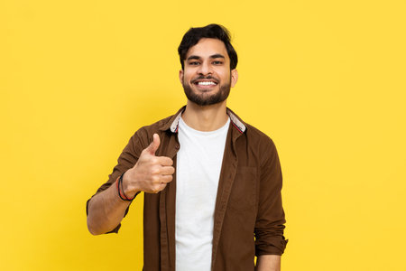 Confident Young Man Giving Thumbs Up on Yellow Backgroundの写真素材