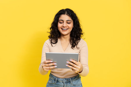 Happy Young Woman Using Tablet On Yellow Backgroundの写真素材