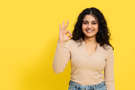 Happy Young Woman Giving Okay Sign on Yellow Backgroundの写真素材