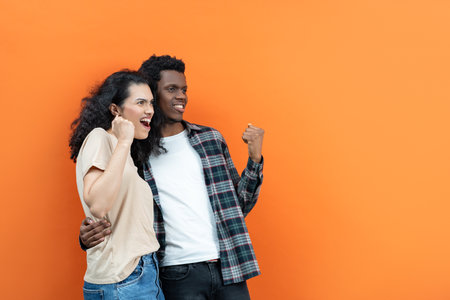 Excited Young Couple Celebrating Success On Orange Backgroundの写真素材
