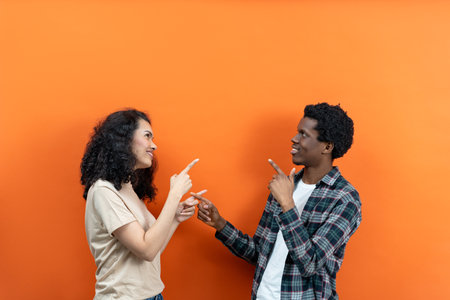 Young Couple Pointing Each Other On Vibrant Orangeの写真素材