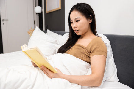 Young Woman Enjoying Reading a Book in Bedの写真素材