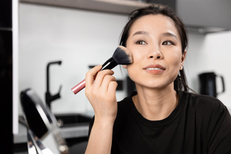 Young Woman Applying Makeup with Brush Indoorsの写真素材