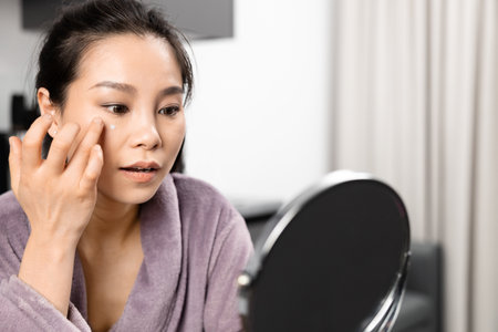 Young Woman Applying Cream in Front of Mirrorの写真素材