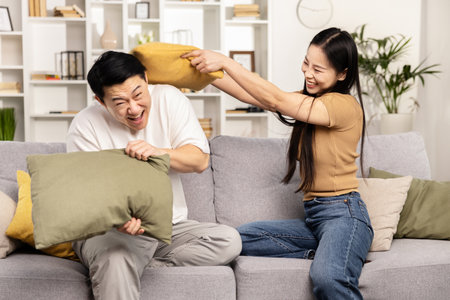Laughing Couple Having Pillow Fight on Sofa at Homeの写真素材