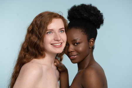 Two Diverse Women Smiling and Embracing on Blue Backgroundの写真素材