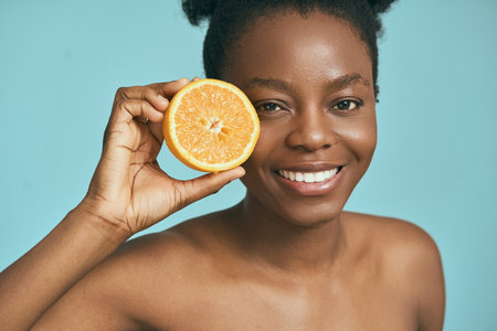 Smiling Woman Holding Orange Slice Against Blue Backgroundの写真素材
