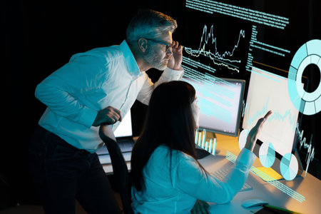 Two Analysts Reviewing Data on Multiple Computer Screens in a Dark Office