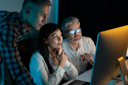 Focused Team Working Late on Computer in Officeの写真素材