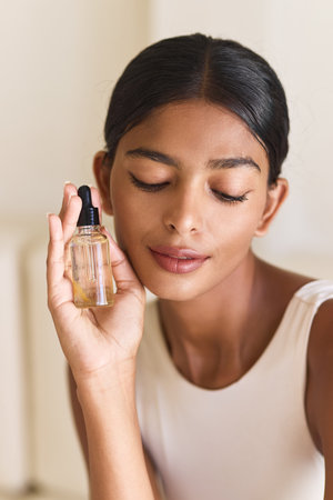 Calm Woman Enjoying Skincare Routine With Facial Oil Bottleの写真素材