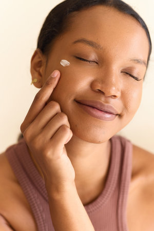 Woman Applying Face Cream Smiling in Skincare and Beauty Routineの写真素材